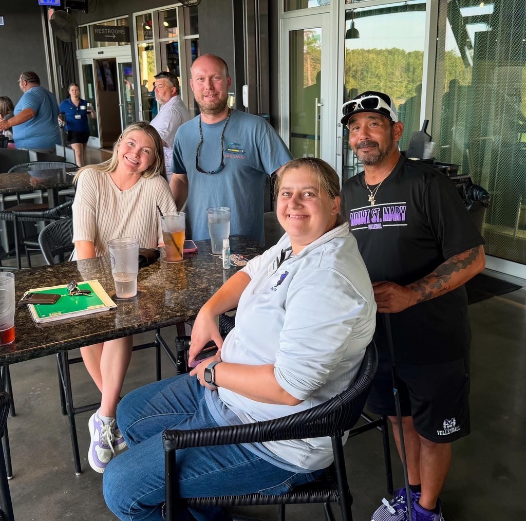 four individuals standing at table on patio and smiling at camera