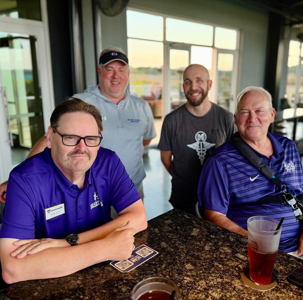 four individuals standing at table on patio and smiling at camera