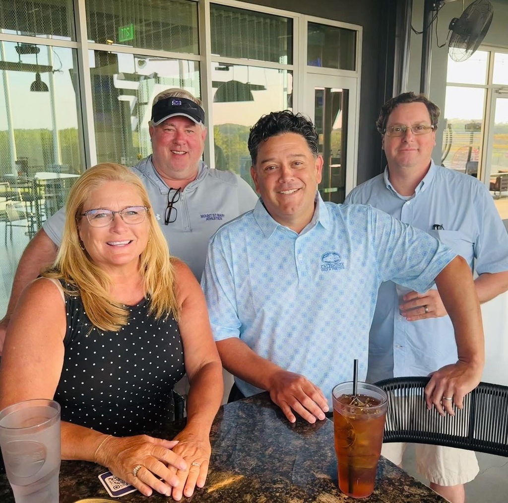 four individuals standing at table on patio and smiling at camera
