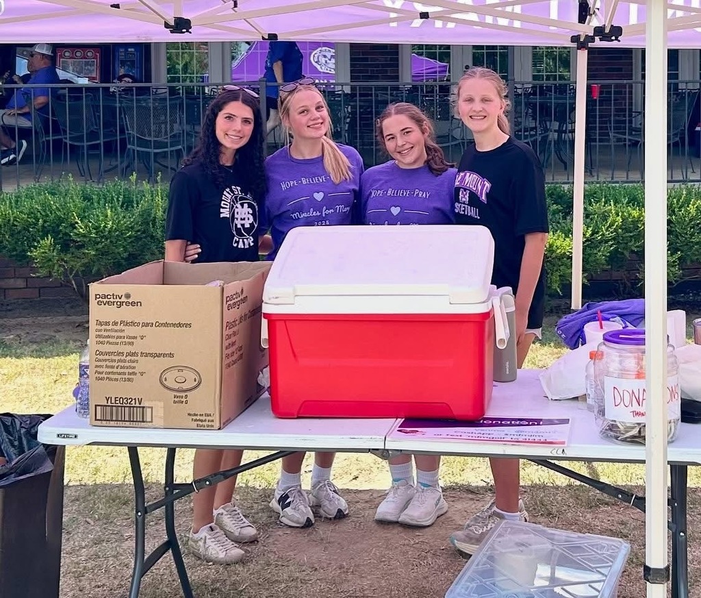 four individuals standing outside under purple tent