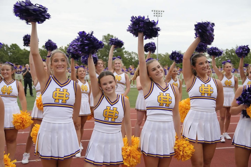 cheerleaders in white, purple and gold uniforms  and with purple and gold poms
