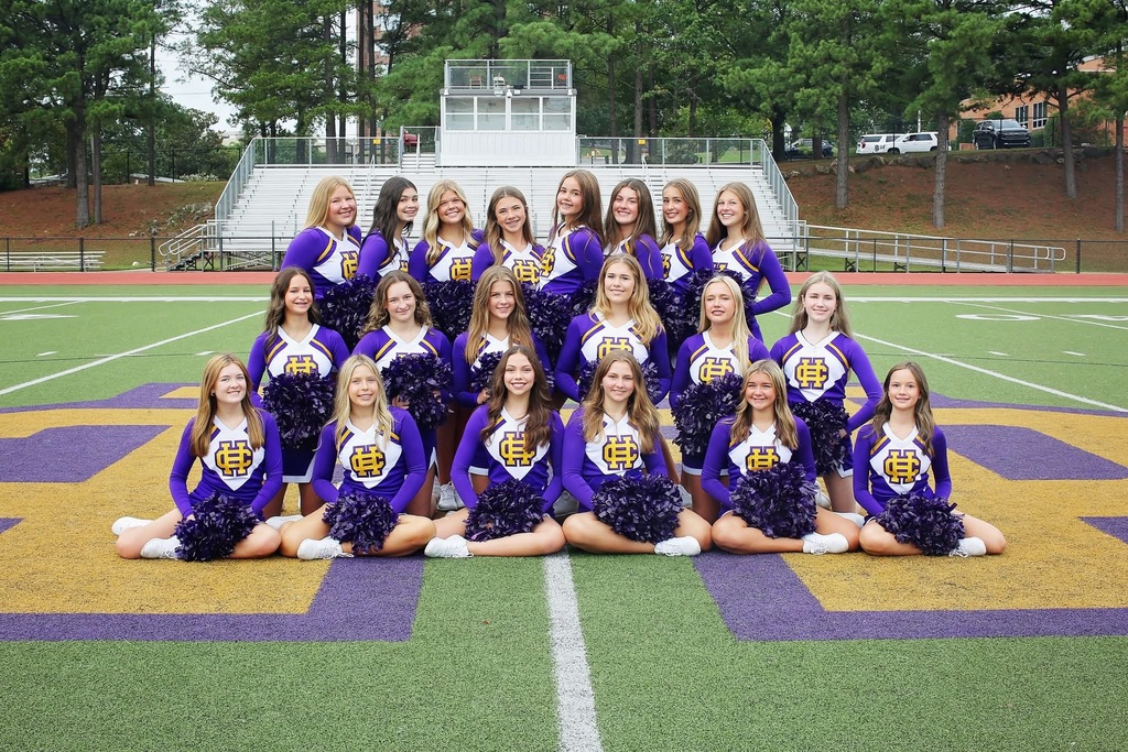 large group of cheerleaders in purple, gold and white uniforms, on a football field