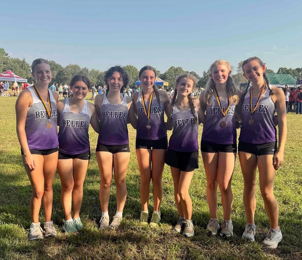 cross country runners standing on large grassy area and smiling at the camera
