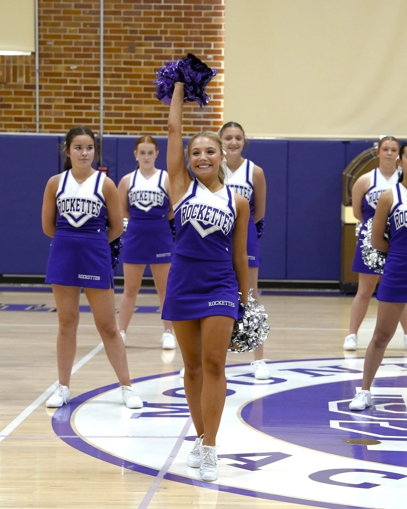 female dance team member in purple and white uniform mid-cheer in gymnasium