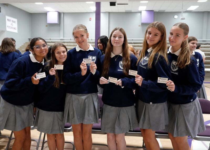 six students holding small Mercy cards and smiling at the camera