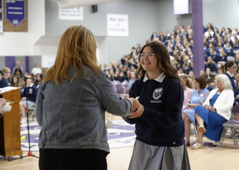 teacher handing a student a small Mercy card