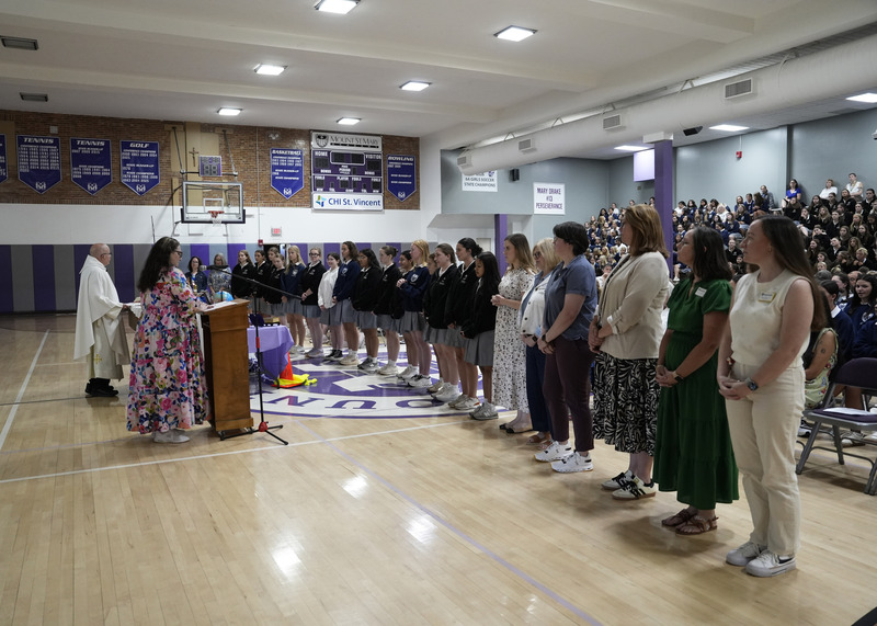 a group of student and faculty standing at the front of an assembly in a gymnasium