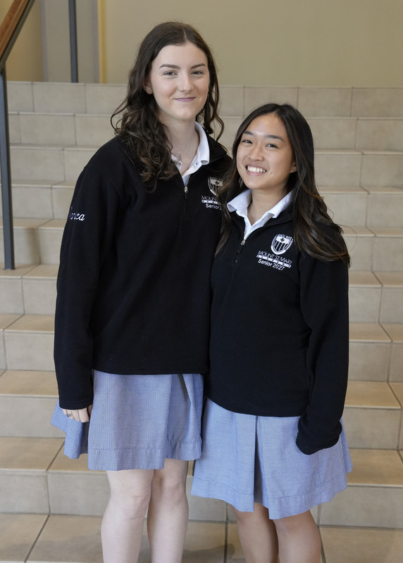 two students standing in front of staircase smiling at the camera
