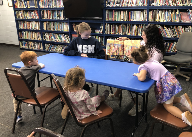 two high school students reading to three elementary school students in a school library