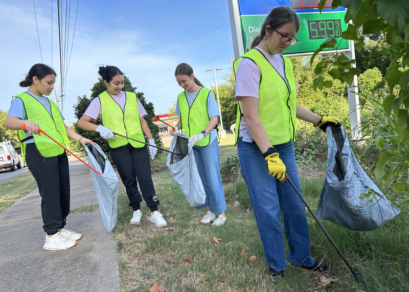 four students picking up trash besides a road