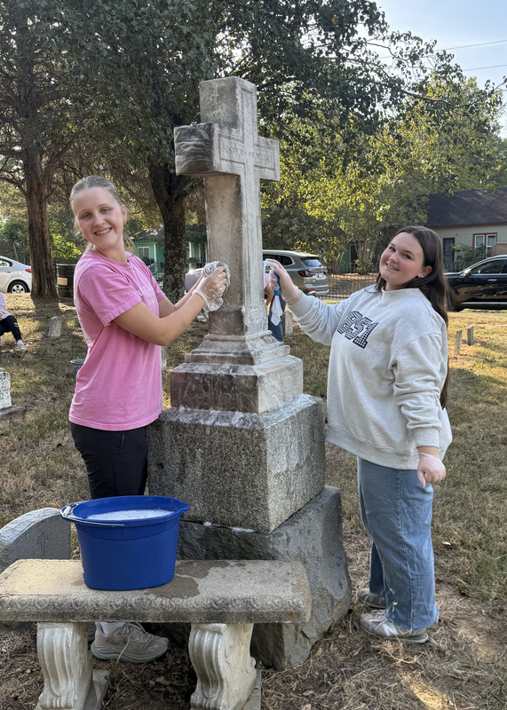 two students cleaning a large headstone in a cemetery