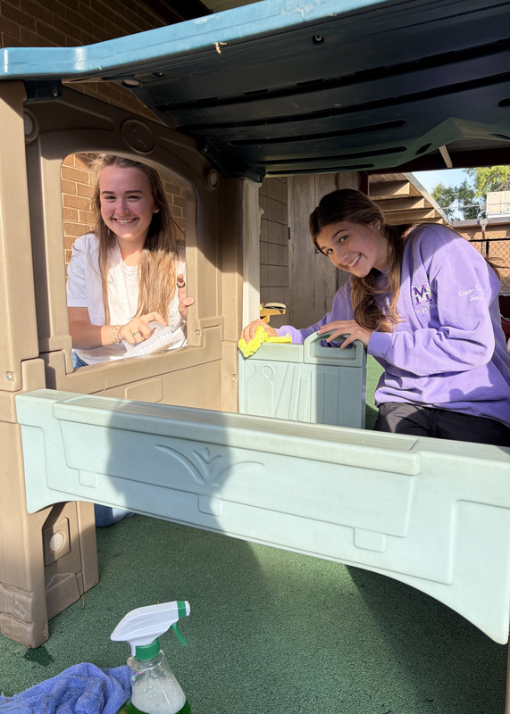 two students cleaning a children's outdoor playset