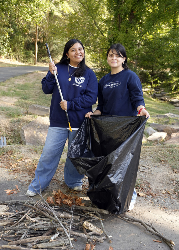 two students in the process of raking up fallen branches