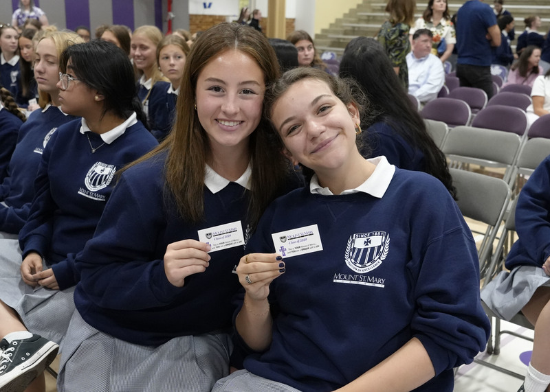 two students holding up their Mercy Cards and smiling at the camera