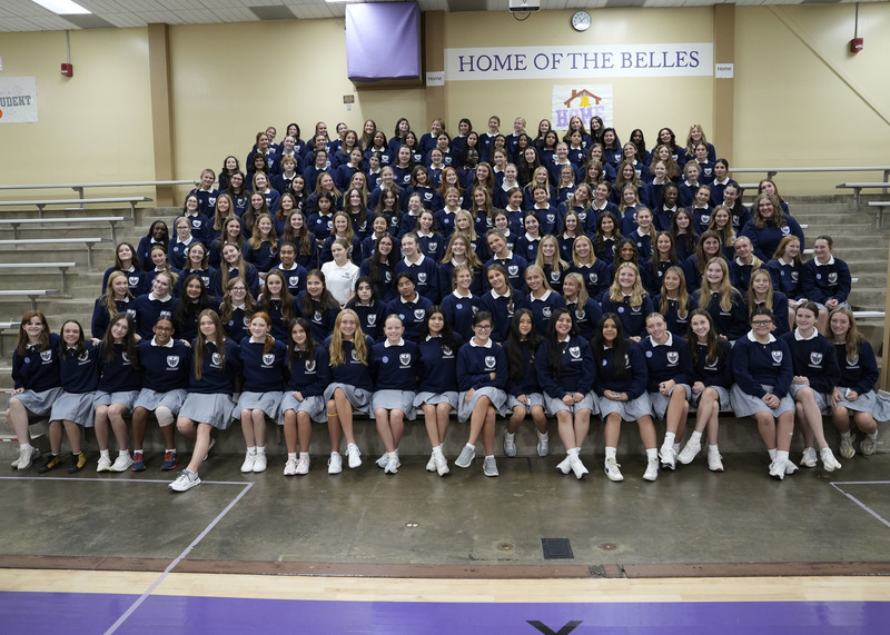 large group of students sitting in the bleachers in a gym and smiling at the camera