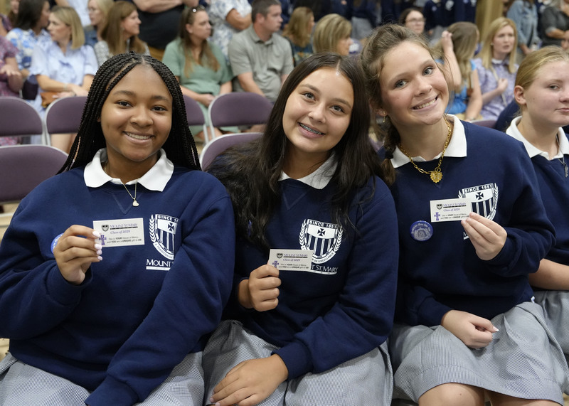 three students holding up their Mercy Cards and smiling at the camera