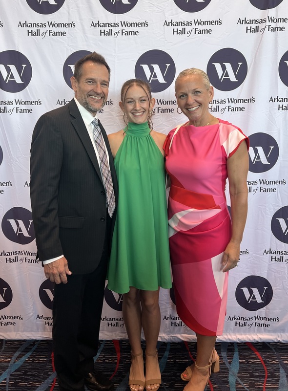 three people standing in front of white banner with Women's Hall of Fame logo repeated across it