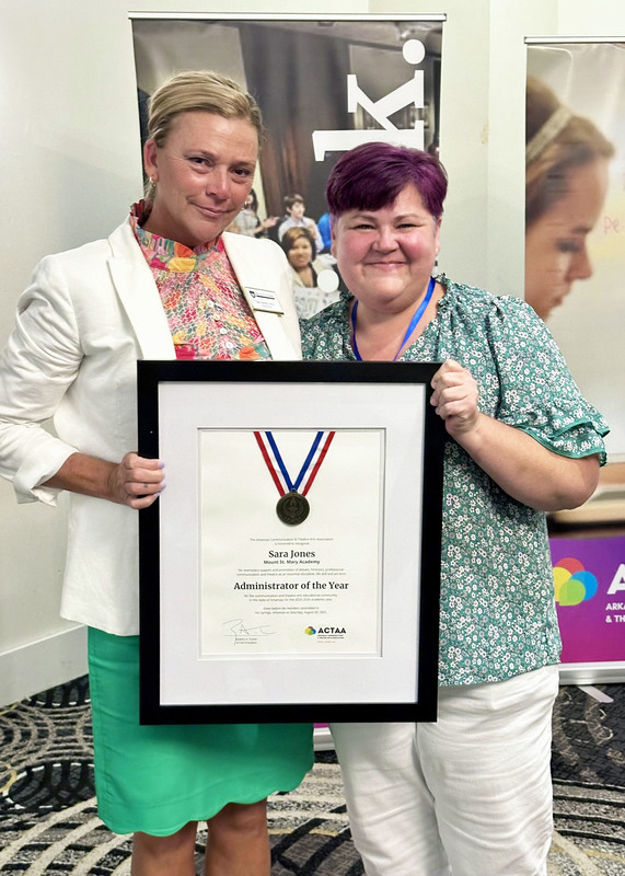 two women smiling at the camera and holding a large framed award