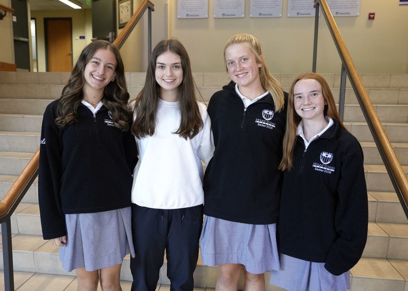 four young women standing in front of staircase in foyer and smiling at camera