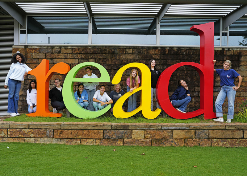 a group of young women standing around a colorful sign saying "read"