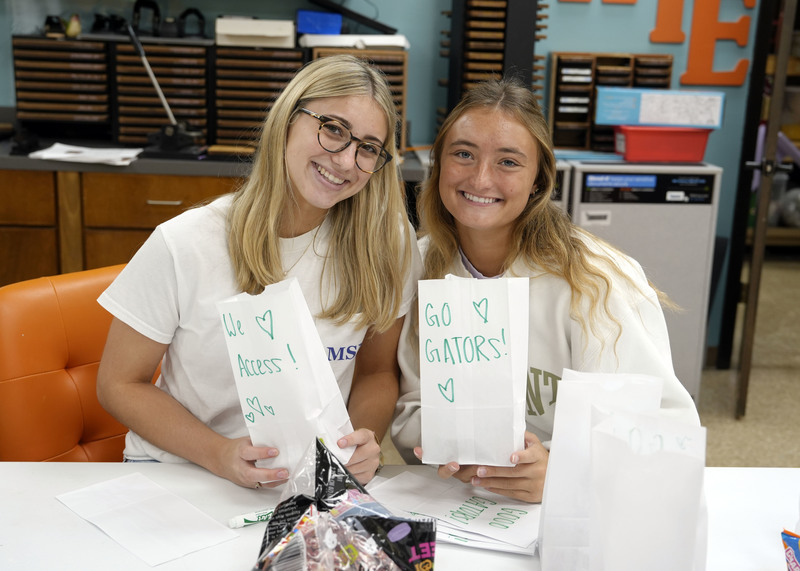two young women holding white paper bags that they've decorated