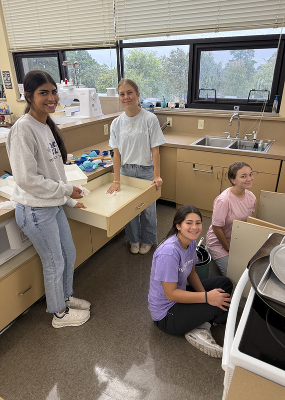 four young women cleaning a kitchenette in a school classroom