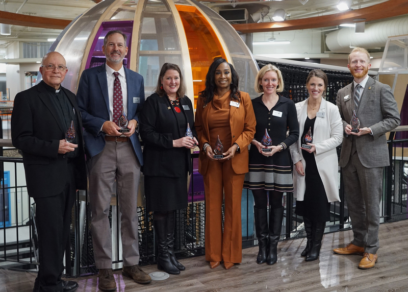 seven individuals smiling at camera while holding award