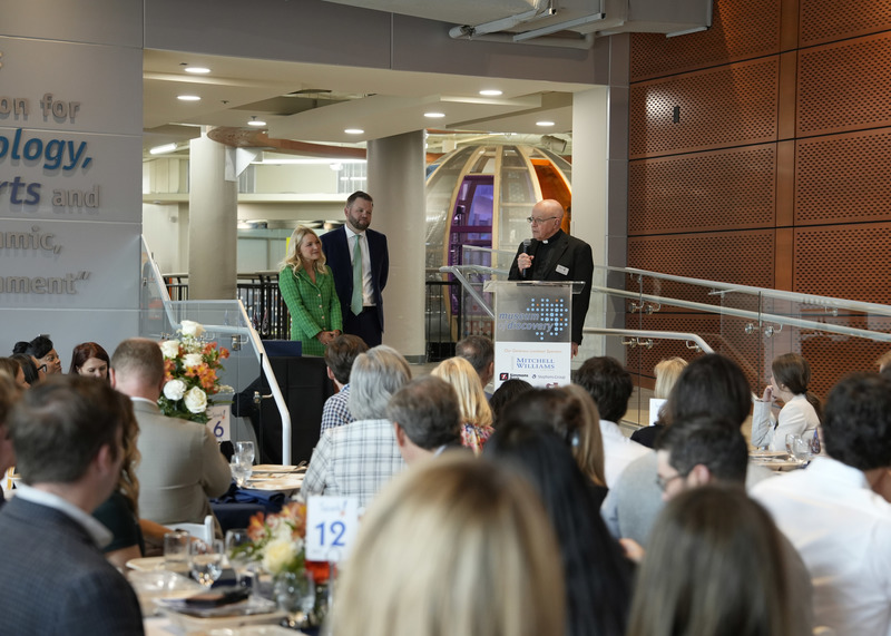 a man standing at a podium giving a speech as others look on