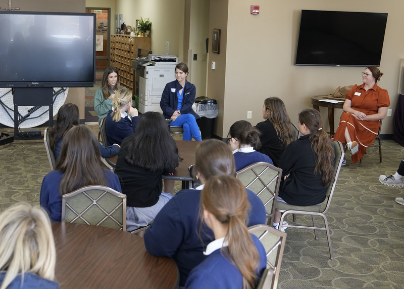 group of three women seated at front of classroom speaking to a group of students