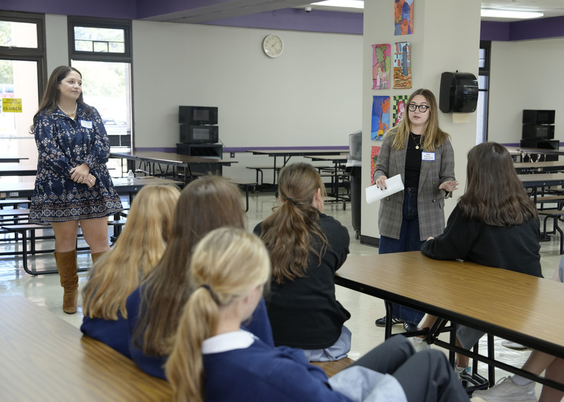 group of two women standing at front of a room speaking to a group of students
