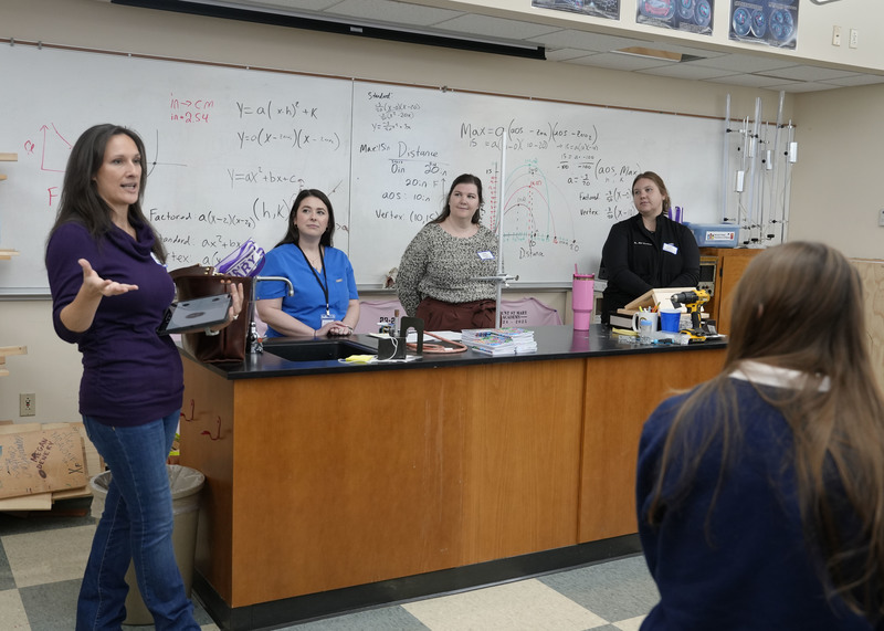 group of four women standing at front of classroom speaking to a group of students