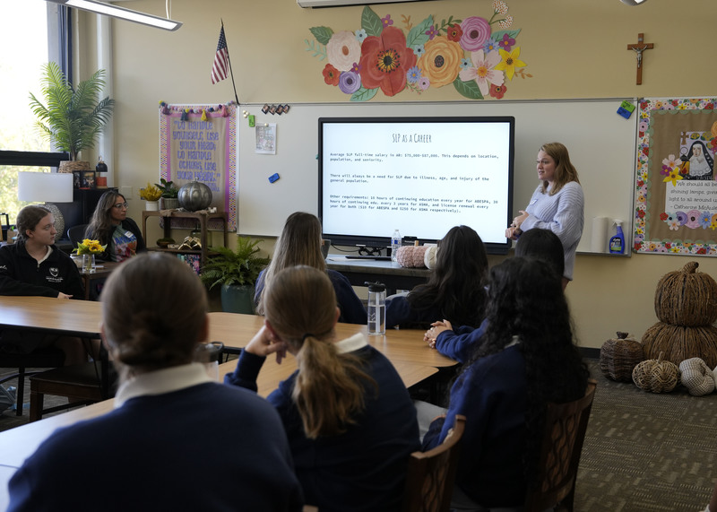 woman standing at front of classroom speaking to a group of students