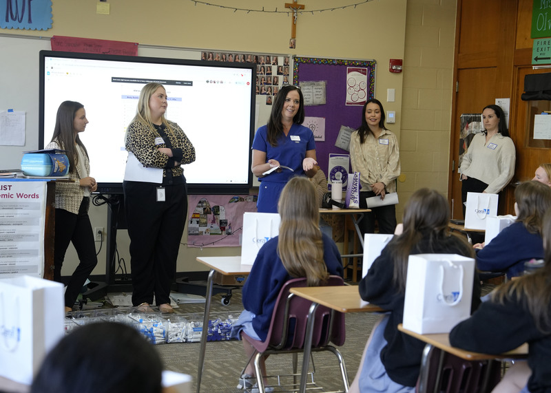 group of five women standing at front of classroom speaking to a group of students