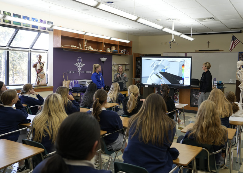 group of three women standing at front of classroom speaking to a group of students