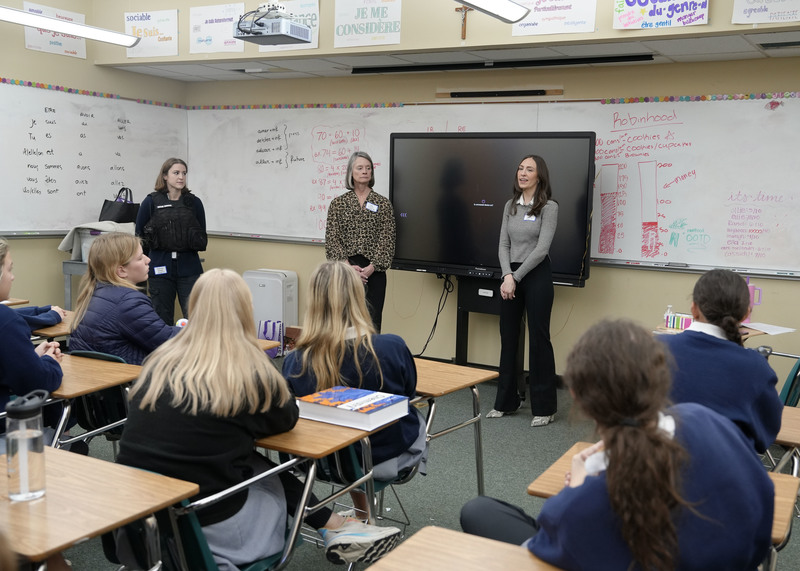 group of three women standing at front of classroom speaking to a group of students