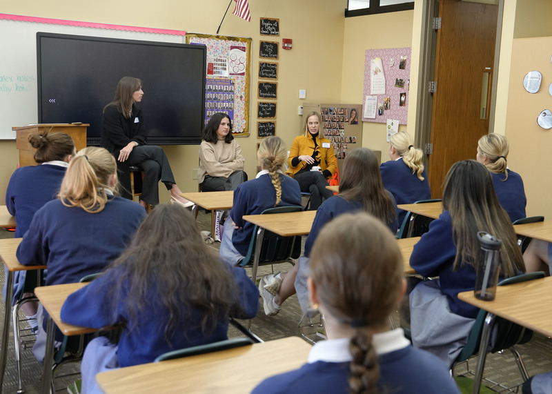 group of three women seated at front of classroom speaking to a group of students