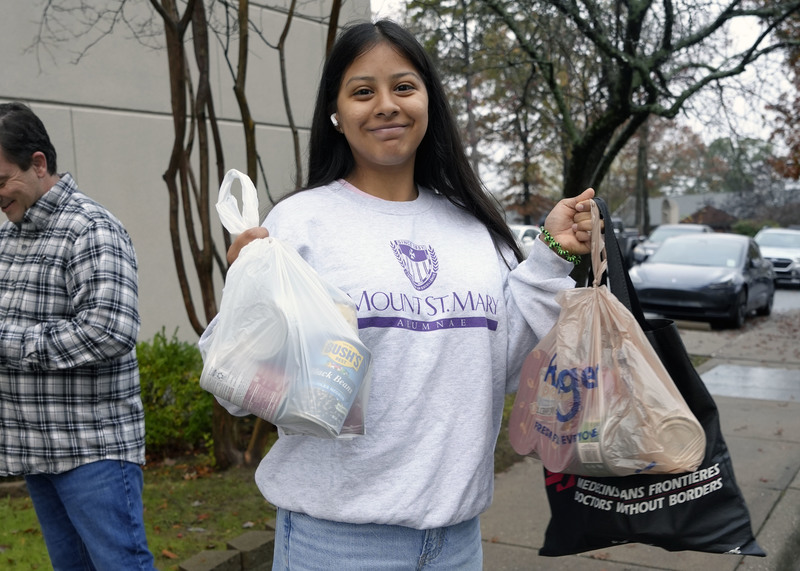 girl holding two bags of plastic bags filled with canned goods