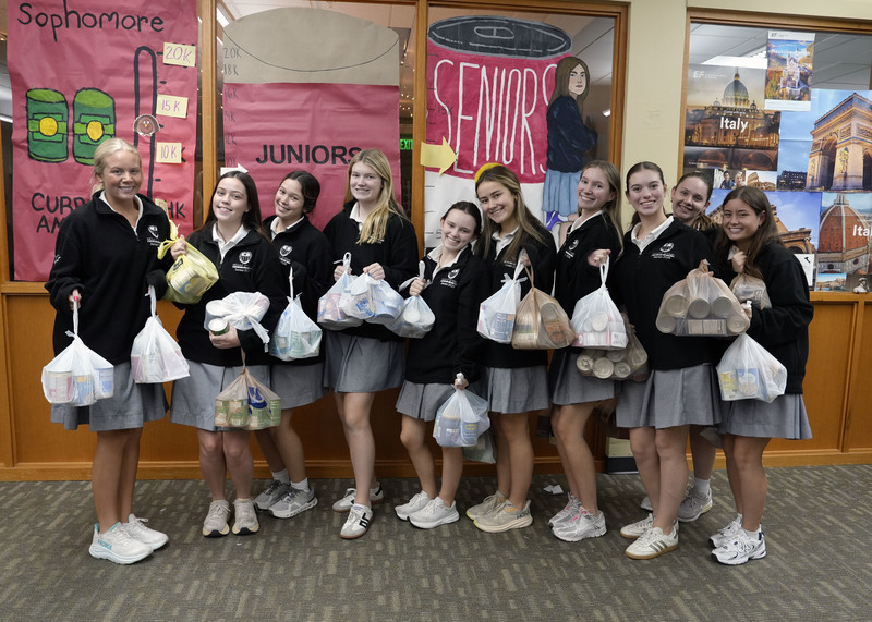 large group of girls standing with boxes and plastic bags of canned goods
