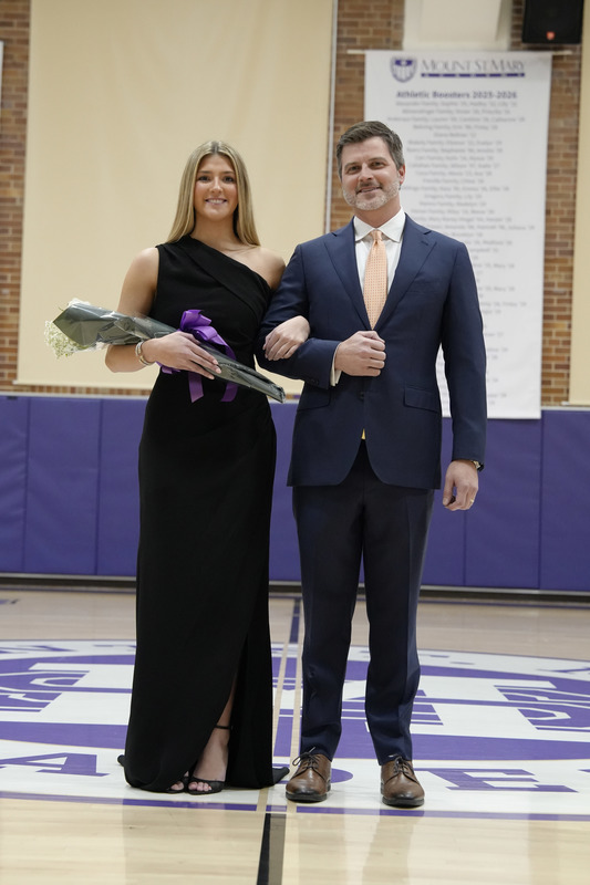 a young women dressed in a formal gown, holding a bouquet of flowers, and being escorted by her father