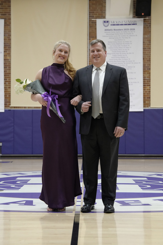 a young women dressed in a formal gown, holding a bouquet of flowers, and being escorted by her father