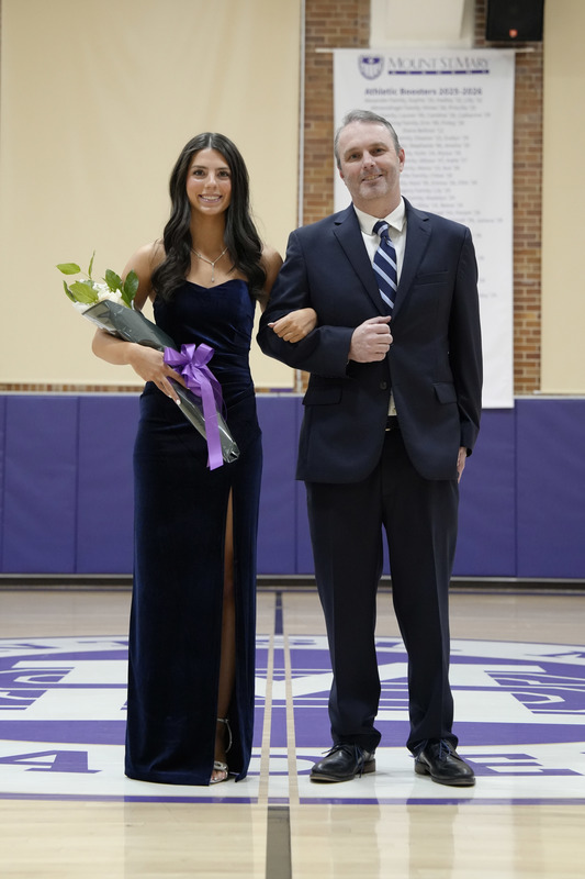 a young women dressed in a formal gown, holding a bouquet of flowers, and being escorted by her father