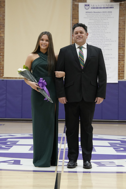 a young women dressed in a formal gown, holding a bouquet of flowers, and being escorted by her father