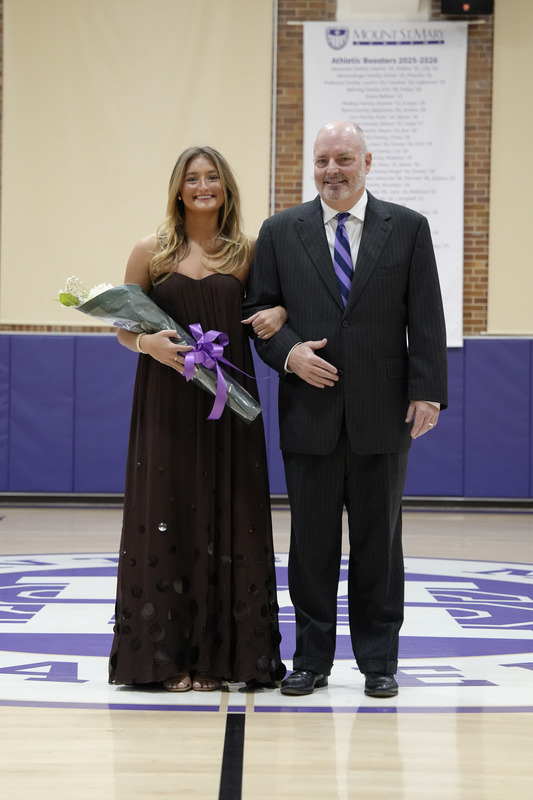 a young women dressed in a formal gown, holding a bouquet of flowers, and being escorted by her father