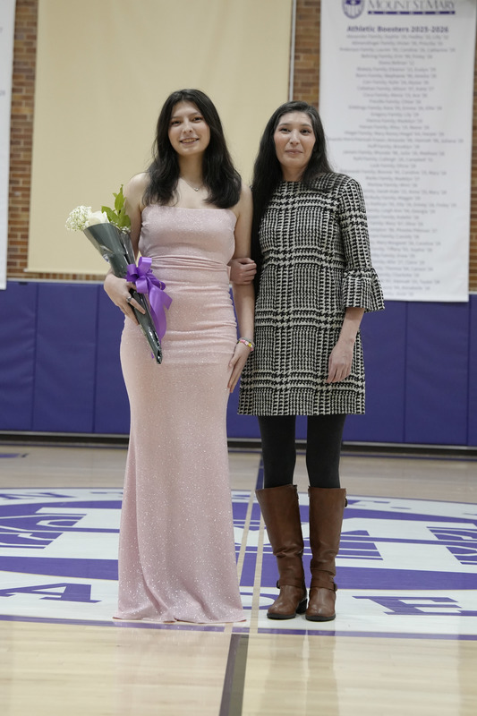 a young women dressed in a formal gown, holding a bouquet of flowers, and being escorted by her mother