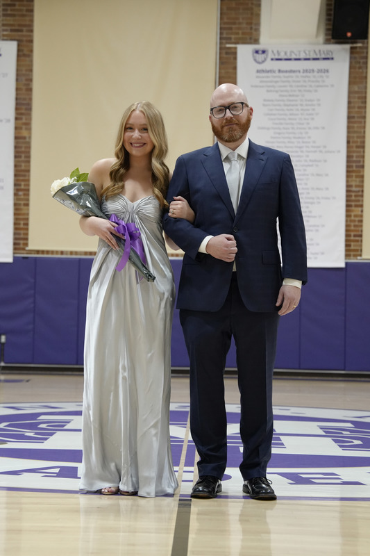 a young women dressed in a formal gown, holding a bouquet of flowers, and being escorted by her father
