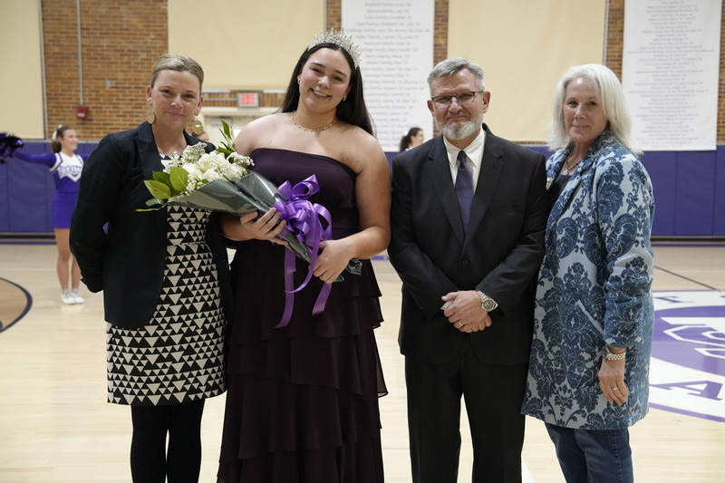 a young women dressed in a formal gown, holding a bouquet of flowers, with her father and two female school administrators standing on both sides