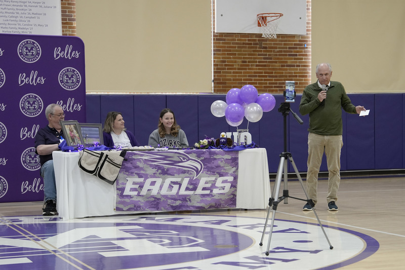 student sitting at decorated table alongside parents while coach is standing nearby and speaking
