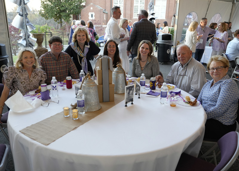 seven guests seated at a table inside the event tent  and smiling for the camera
