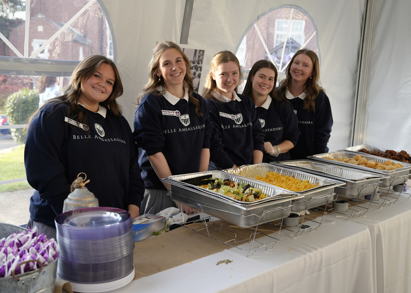 five students in uniform standing behind the buffet line of food prepared to serve