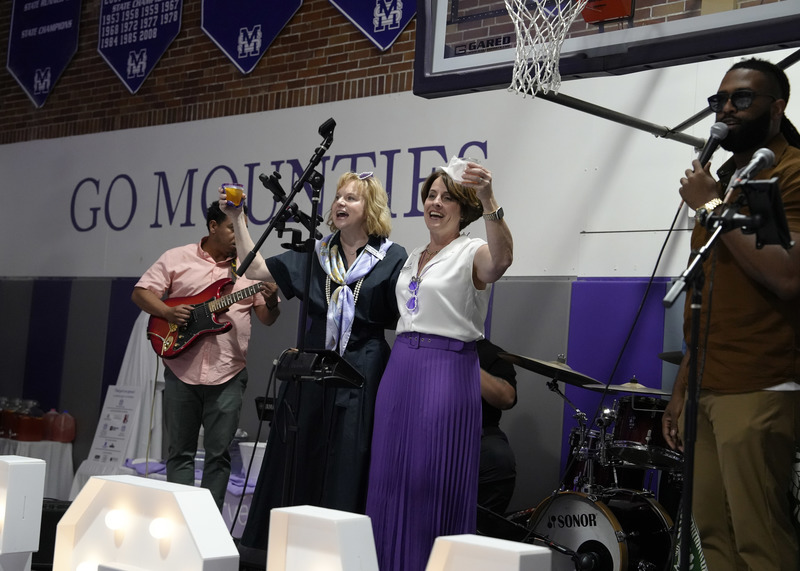 two individuals standing on a stage mid celebratory toast alongside a couple band members